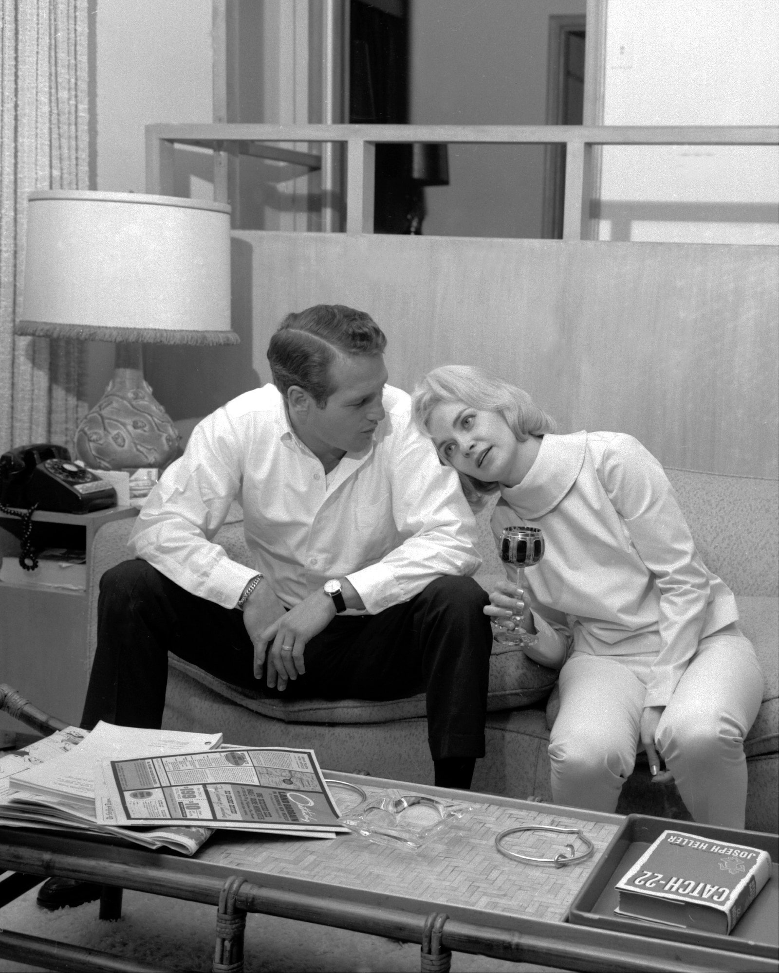 Paul Newman left and Joanne Woodward sitting on a sofa coffee table in front of them with newspapers a copy of Catch22